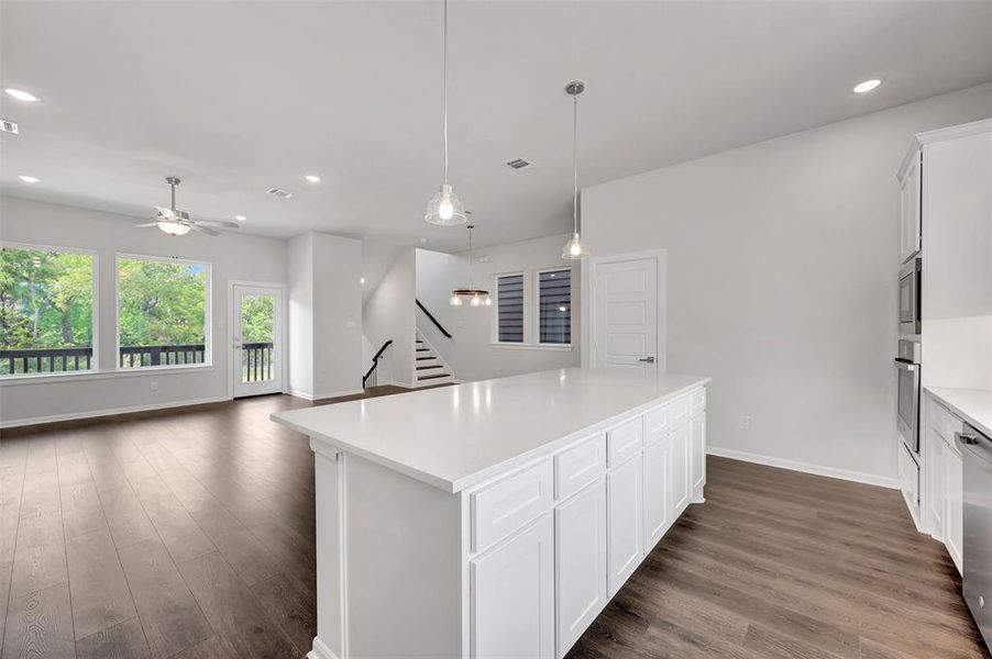 Spacious kitchen island with a light-toned countertop, white cabinetry, wood-finish flooring, recessed lighting, and a modern ceiling fan