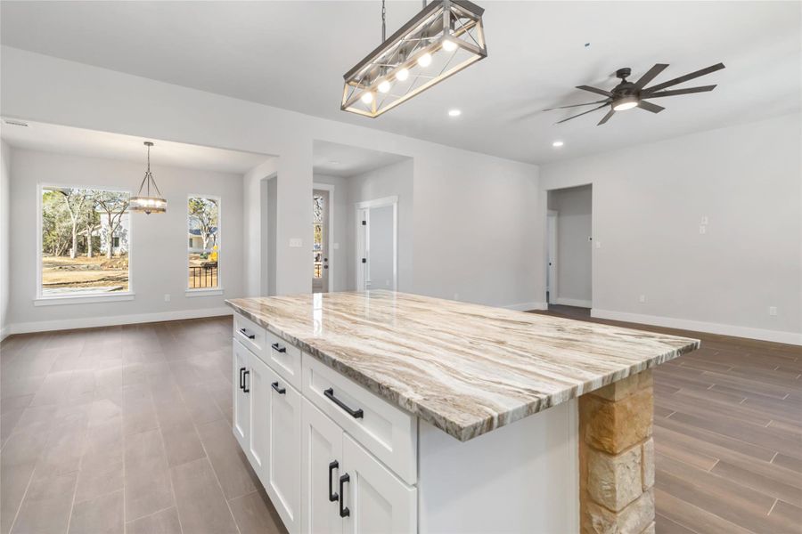 Kitchen with hanging light fixtures, light stone countertops, a center island, and white cabinets