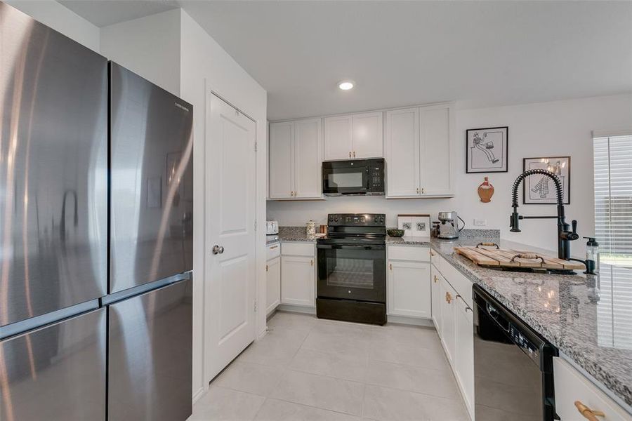 Kitchen with black appliances, light stone countertops, white cabinetry, recessed lighting, and light tile patterned floors Kitchen with black appliances, light stone countertops, white cabinetry, recessed lighting, and light tile patterned floors
