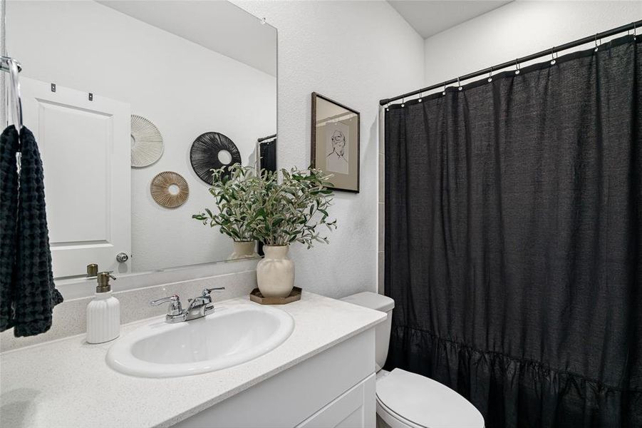Bathroom featuring a vanity with a white countertop and an integrated sink, a toilet, and a shower with a dark curtain