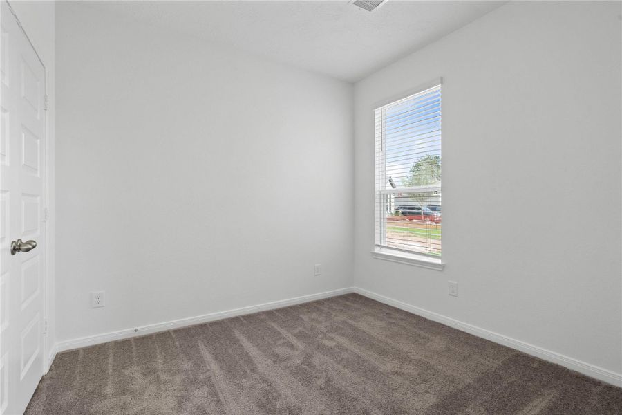 This secondary bedroom offers comfort and style with plush carpet flooring, neutral paint tones, a large window with blinds, and ample sized closet space.