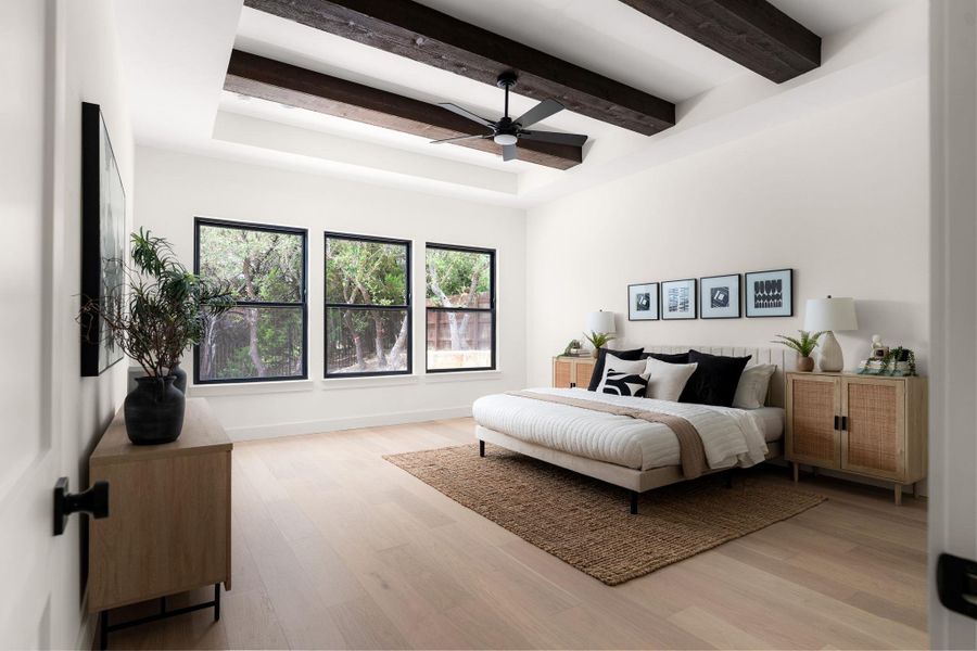 Exposed wood beams frame the tray ceiling of this sun-filled bedroom, complete with rich hardwood floors.