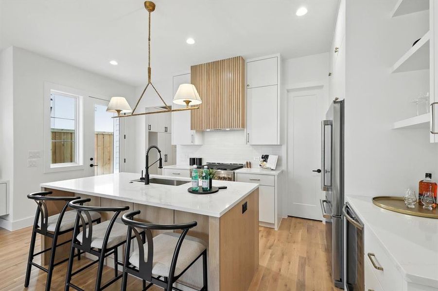 Kitchen featuring white cabinetry, an island with sink, light wood-type flooring, a kitchen bar, and light stone countertops Kitchen featuring white cabinetry, an island with sink, light wood-type flooring, a kitchen bar, and light stone countertops