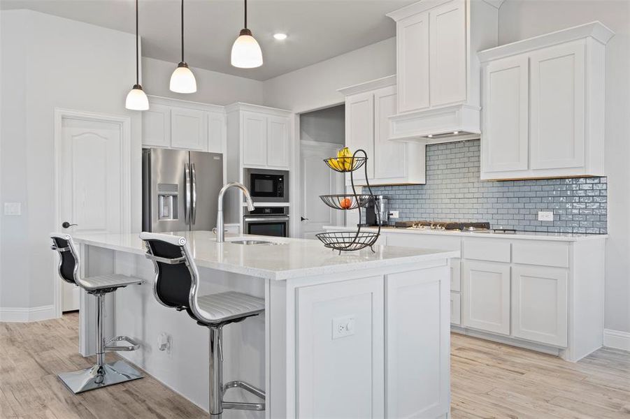 Kitchen with backsplash, sink, appliances with stainless steel finishes, light hardwood / wood-style flooring, and an island with sink