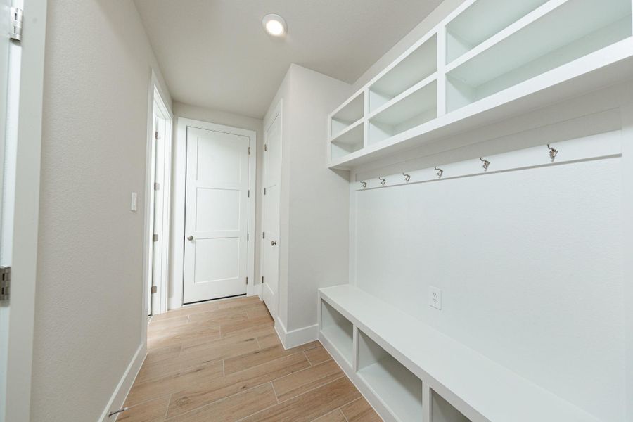 Step into this highly functional and stylish mudroom drop zone, an essential feature for a busy household. The space boasts custom-built white cabinetry and shelving, providing generous storage for coats, bags, and shoes. A comfortable built-in bench offers a convenient spot to sit, while three sleek hooks keep outerwear tidy and accessible.