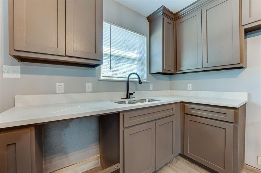 Kitchen with light stone counters, gray cabinets, sink, and light wood-type flooring