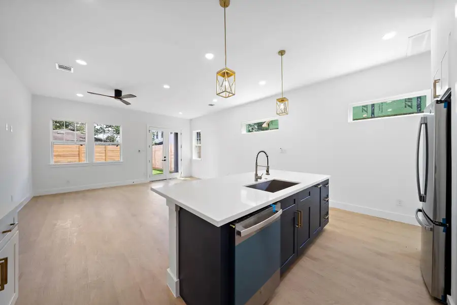 This photo showcases a modern, open-concept living space with a spacious kitchen island featuring a sleek sink and contemporary lighting. The room is bright with light LVP flooring, large windows, and a door leading to a fenced backyard. An overhead fan and recessed lighting add to the modern feel. This photo showcases a modern, open-concept living space with a spacious kitchen island featuring a sleek sink and contemporary lighting. The room is bright with light LVP flooring, large windows, and a door leading to a fenced backyard. An overhead fan and recessed lighting add to the modern feel.