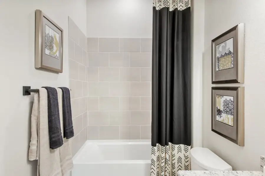 Bathroom with soaking tub, tiled surround, black and white shower curtain, and towel bar with folded towels