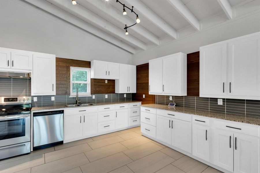Kitchen with stainless steel appliances, a sink, dark stone counters, and backsplash