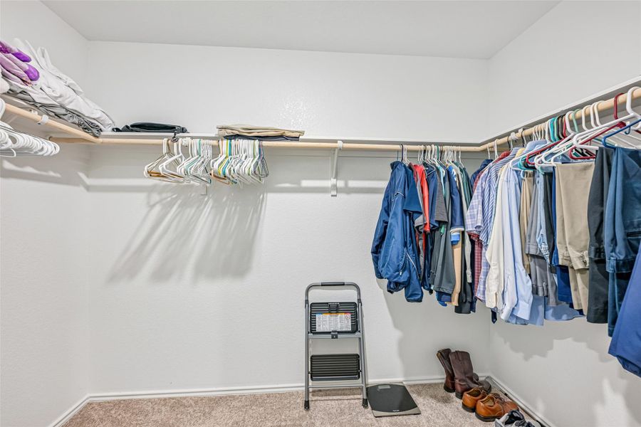 Walk-in closet featuring carpet flooring, built-in shelving, and multiple hanging rods for ample storage Walk-in closet featuring carpet flooring, built-in shelving, and multiple hanging rods for ample storage