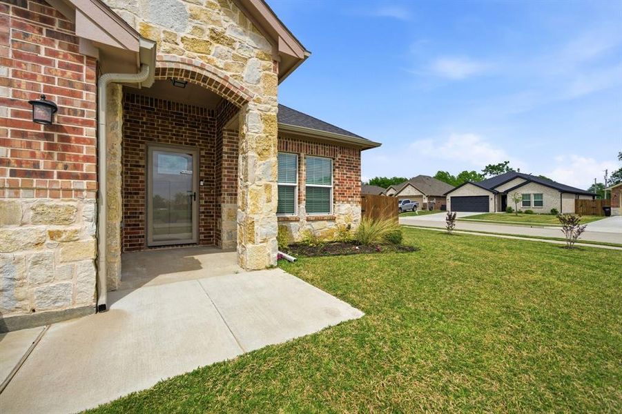 View of exterior entry featuring stone siding, a yard, and brick siding
