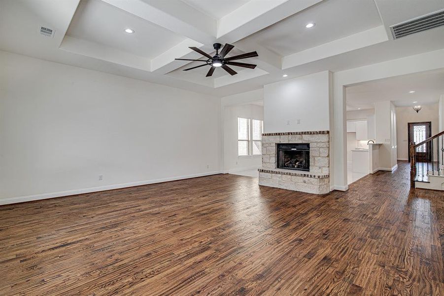 Unfurnished living room featuring coffered ceiling, ceiling fan, dark hardwood / wood-style floors, a fireplace, and beamed ceiling