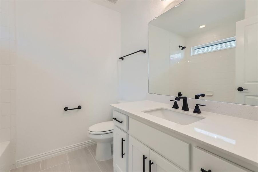 Full bathroom with tiled shower / bath combo, tile flooring, toilet, and large vanity