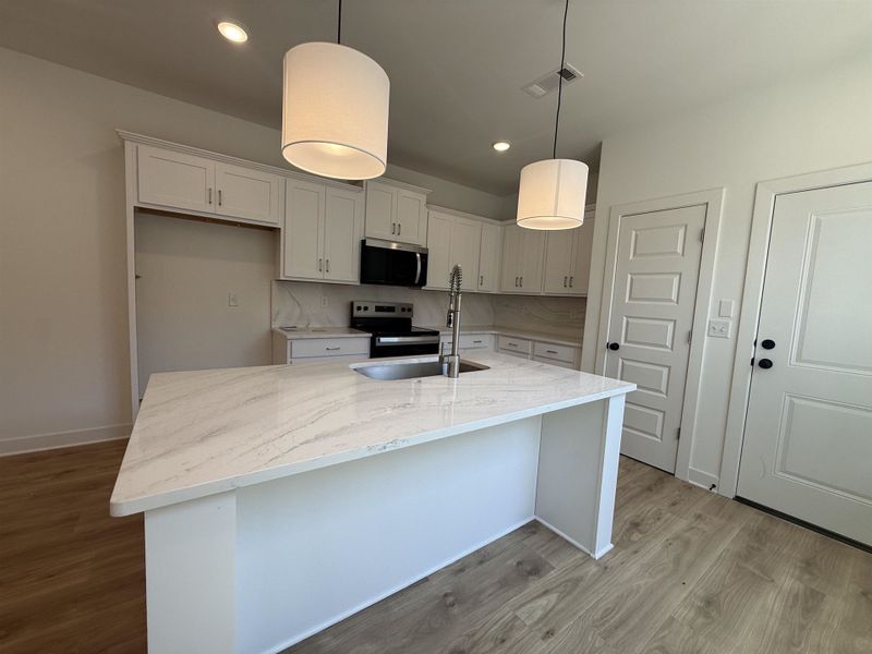 Kitchen featuring light stone countertops, stainless steel appliances, light wood-type flooring, a kitchen island with sink, and decorative light fixtures