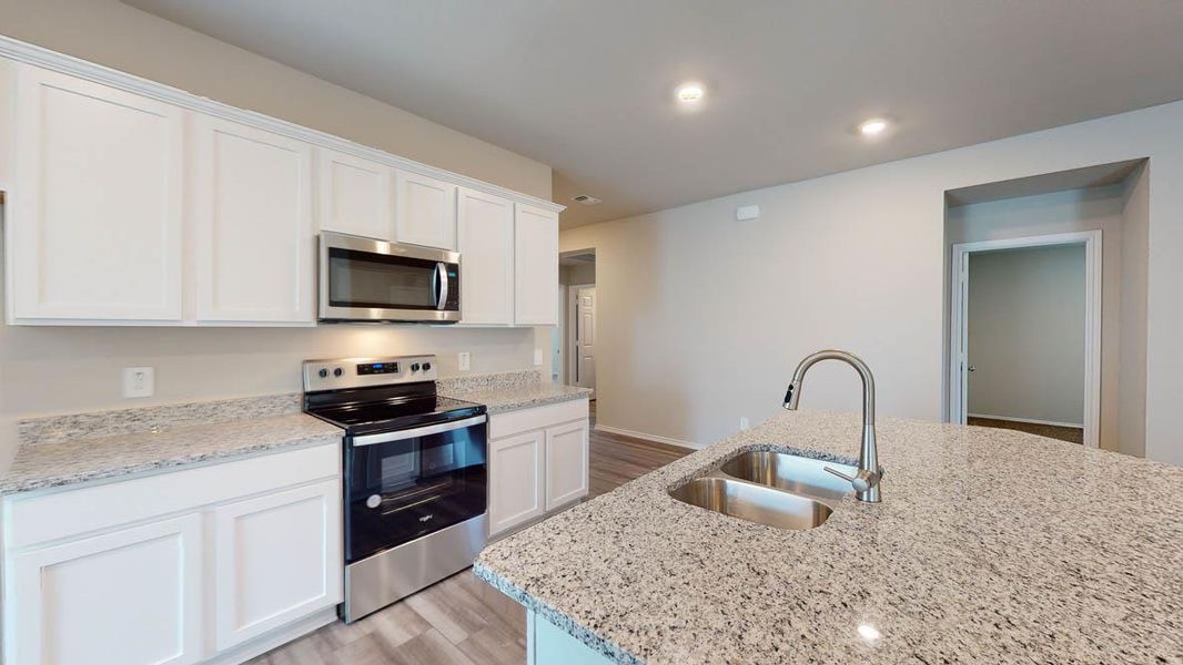Kitchen with stainless steel appliances, white cabinetry, light wood finished floors, light stone countertops, and recessed lighting
