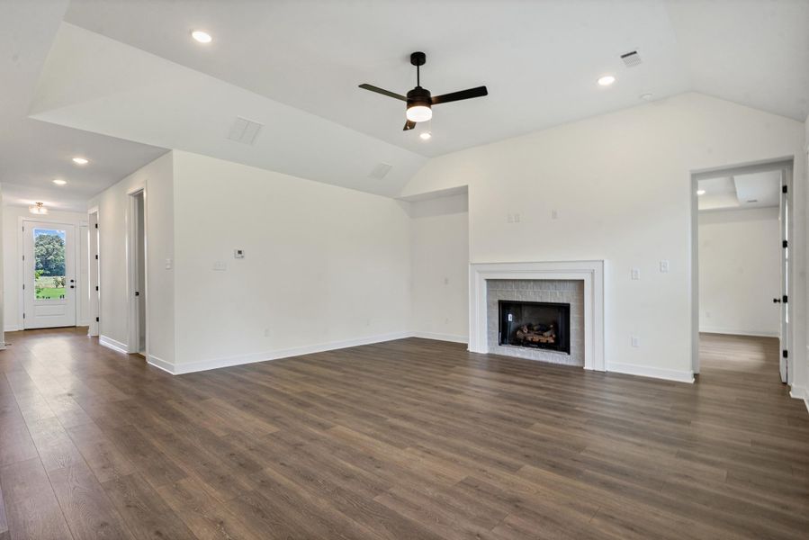Spacious living area featuring wood-finish flooring, a white mantel fireplace with tile surround, vaulted ceilings, recessed lighting, and a ceiling fan Spacious living area featuring wood-finish flooring, a white mantel fireplace with tile surround, vaulted ceilings, recessed lighting, and a ceiling fan