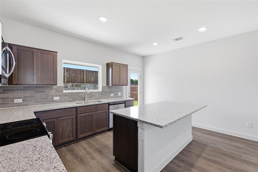 Modern kitchen featuring recessed lighting, wood-finish flooring, dark wood cabinetry, light-toned countertops, and a subway tile backsplash