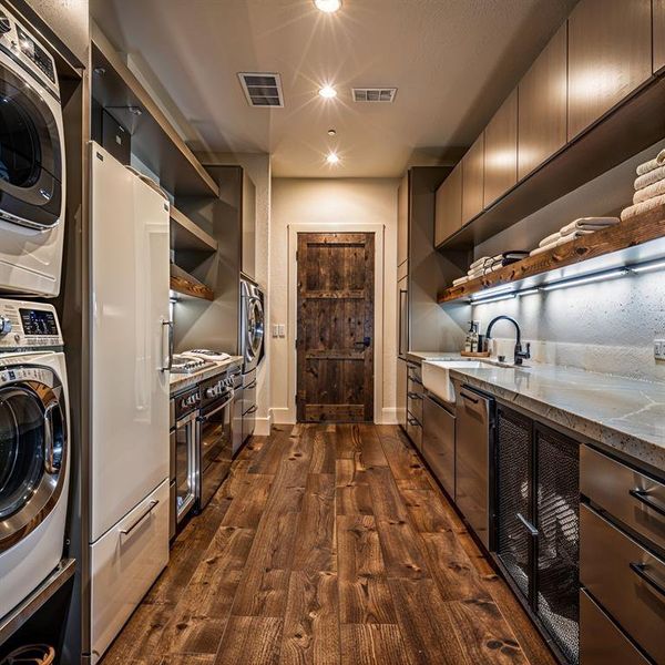 Washroom featuring visible vents, dark wood finished floors, laundry area, stacked washing maching and dryer, and a sink