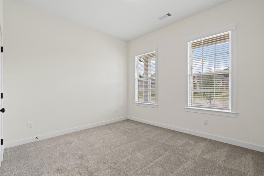Bright room featuring two double-hung windows with blinds, light gray carpet, and white walls with matching trim Bright room featuring two double-hung windows with blinds, light gray carpet, and white walls with matching trim