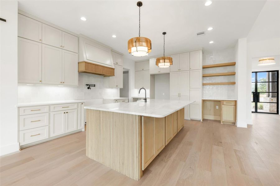 Kitchen featuring a center island with sink, light stone countertops, light wood-style flooring, a breakfast bar area, and open shelves