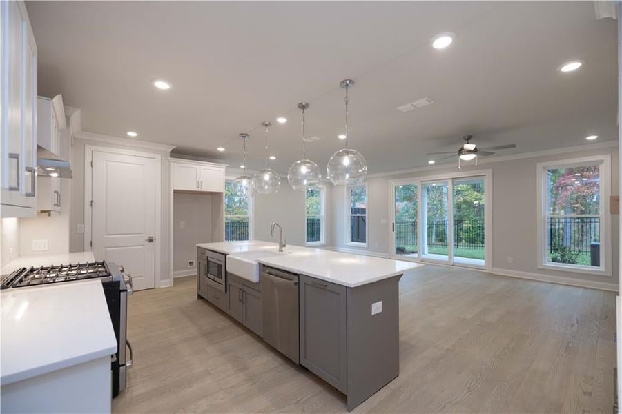 Kitchen featuring crown molding, an island with sink, pendant lighting, stainless steel appliances, and white cabinets