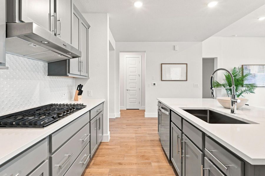 Close-up of the kitchen workspace showcasing straight bar pulls in chrome, 36" gas cooktop, and seamless Silestone counter prep space. Close-up of the kitchen workspace showcasing straight bar pulls in chrome, 36" gas cooktop, and seamless Silestone counter prep space.