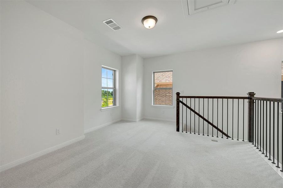 Spacious carpeted loft area with iron baluster railing and dark wood newel posts