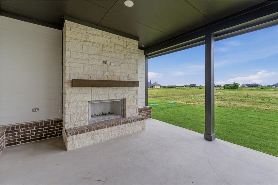 Covered patio featuring an outdoor stone fireplace with a wood mantel