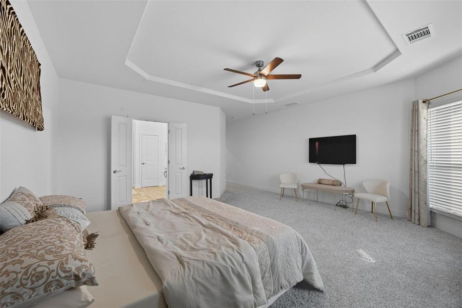 Bedroom with a tray ceiling, light carpet, and a ceiling fan Bedroom with a tray ceiling, light carpet, and a ceiling fan