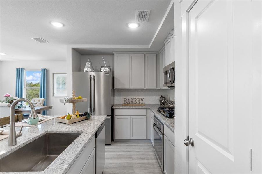 Kitchen with light stone counters, light wood-type flooring, sink, and appliances with stainless steel finishes