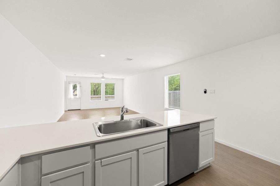 View from the kitchen showcases the open layout extending into the living area, with a generous peninsula, coordinated flooring, and multiple windows bringing in natural light. View from the kitchen showcases the open layout extending into the living area, with a generous peninsula, coordinated flooring, and multiple windows bringing in natural light.