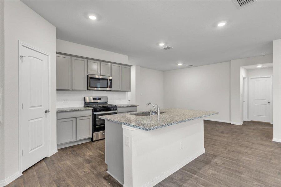 The kitchen features grey cabinetry, stainless steel appliances, and an island with a granite countertop and a sink
