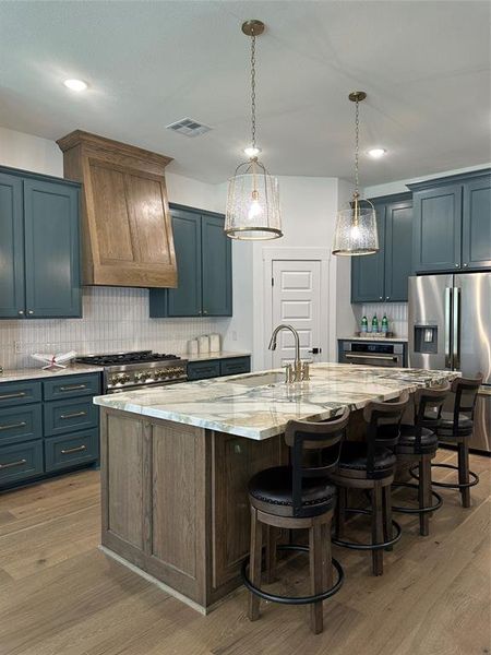 Gourmet kitchen featuring a large island with seating, a professional-grade range, stainless steel appliances, custom cabinetry, and wood-finish flooring