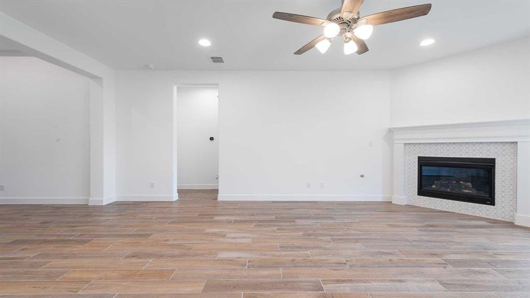 Unfurnished living room with ceiling fan, light wood-type flooring, and a tile fireplace