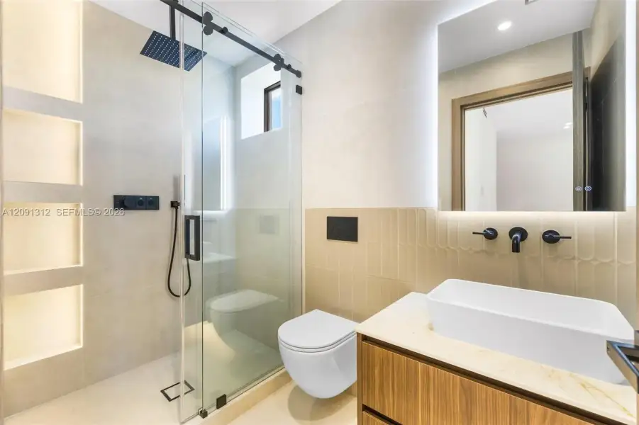 Modern bathroom featuring a wood-finish floating vanity, vessel sink with matte black wall-mounted faucet, wall-mounted toilet, and glass-enclosed shower with integrated recessed shelving Modern bathroom featuring a wood-finish floating vanity, vessel sink with matte black wall-mounted faucet, wall-mounted toilet, and glass-enclosed shower with integrated recessed shelving