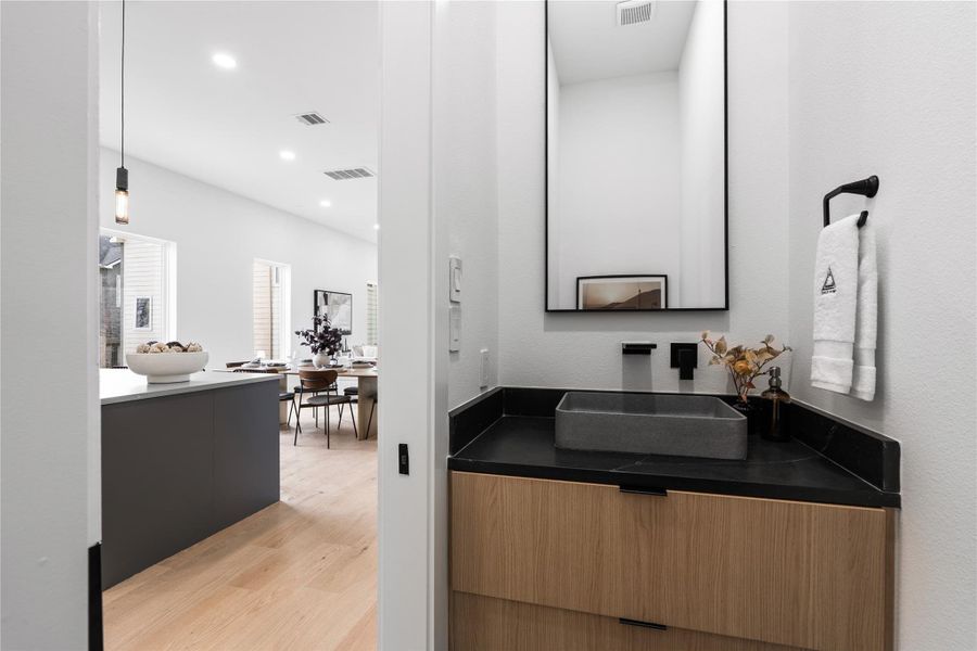 A meticulously composed powder room where form follows precision: clerestory light skims crisp walls, a graphite-hued vessel sink rests on tailored wood cabinetry, and matte-black fixtures punctuate the palette.The herringbone floor adds quiet movement underfoot—an elegant, guest-facing moment that reflects the home’s considered craftsmanship.