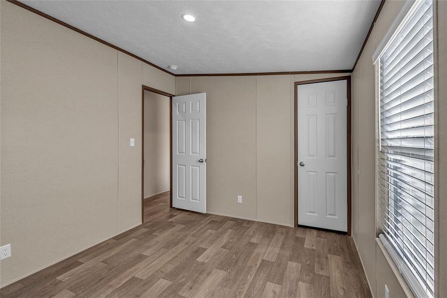 Unfurnished bedroom featuring vaulted ceiling, ornamental molding, and light hardwood / wood-style floors