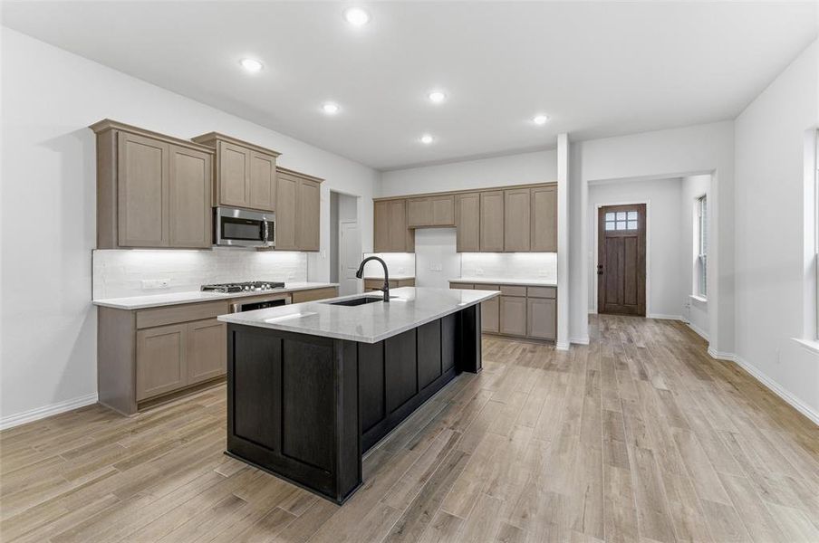 Kitchen featuring a large island with a sink, stainless steel microwave, gas range, wood-finish flooring, and recessed lighting