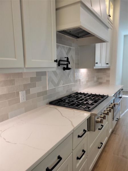 Modern kitchen with sleek white cabinetry, elegant quartz countertops, and a state-of-the-art CAFE gas cooktop. The neutral tile backsplash features a stylish herringbone design, complemented by a convenient pot filler above the stove. Perfect for culinary enthusiasts. Modern kitchen with sleek white cabinetry, elegant quartz countertops, and a state-of-the-art CAFE gas cooktop. The neutral tile backsplash features a stylish herringbone design, complemented by a convenient pot filler above the stove. Perfect for culinary enthusiasts.