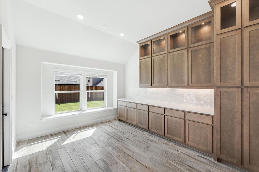 Kitchen with tall brown cabinets, white countertop, subway tile backsplash, and light wood-look floors