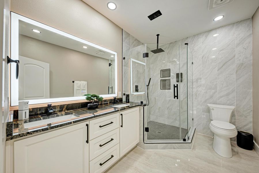 Polished tile surrounds a glass-enclosed walk-in shower alongside a stone-topped double vanity. Polished tile surrounds a glass-enclosed walk-in shower alongside a stone-topped double vanity.