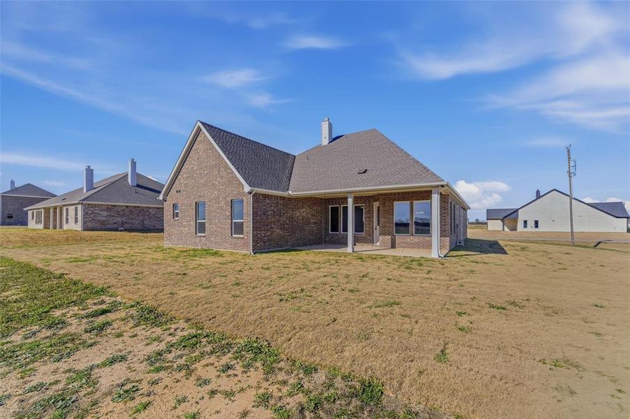 Rear view of property with a patio, a lawn, brick siding, a shingled roof, and a chimney