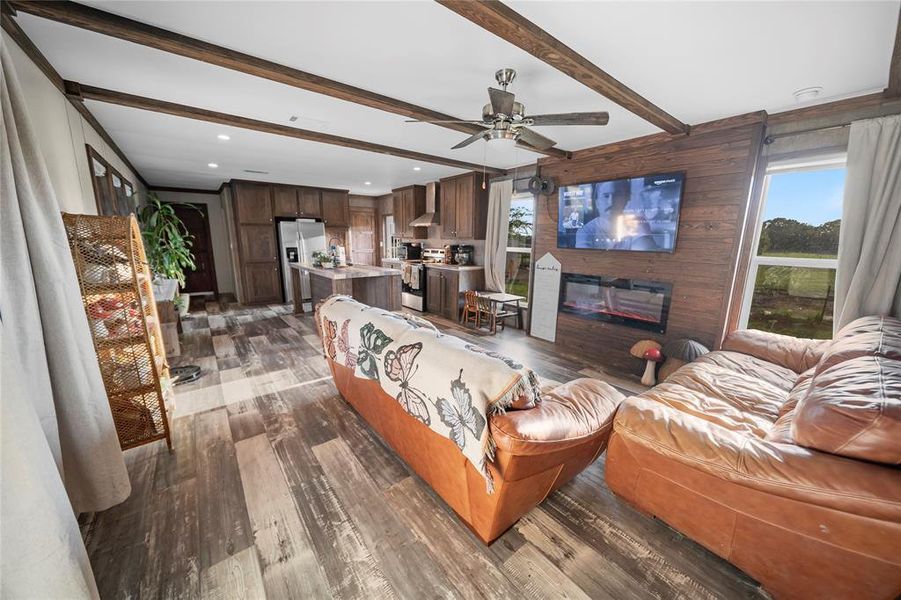 Living area with beamed ceiling, dark wood finished floors, wooden walls, a glass covered fireplace, and ceiling fan Living area with beamed ceiling, dark wood finished floors, wooden walls, a glass covered fireplace, and ceiling fan