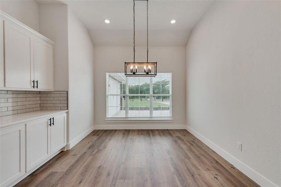 Unfurnished dining area with an inviting chandelier, light wood-type flooring, and lofted ceiling