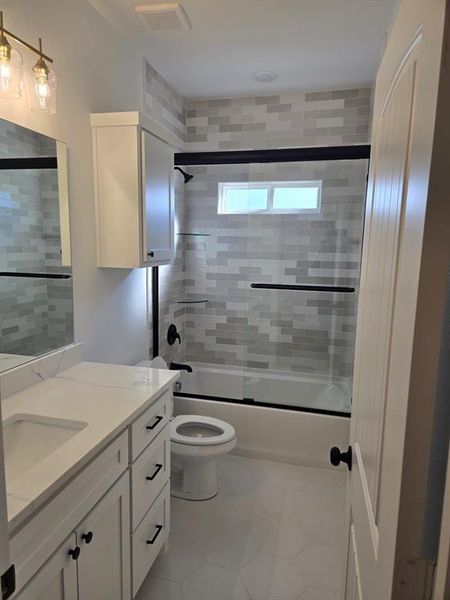 Bathroom featuring vanity, bath / shower combo with glass door, and light tile patterned flooring