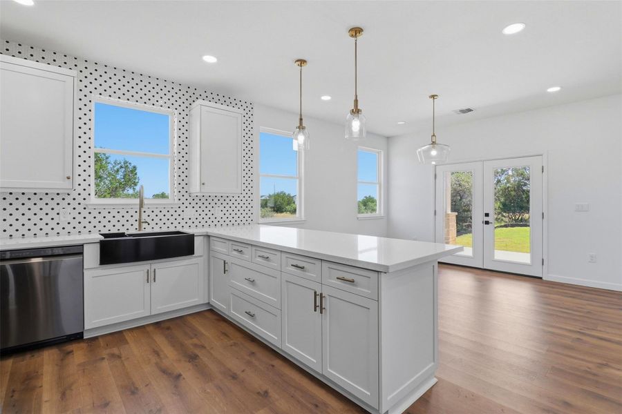 Modern kitchen featuring white shaker cabinetry, an expansive center island with a light-toned countertop, and a black farmhouse sink Modern kitchen featuring white shaker cabinetry, an expansive center island with a light-toned countertop, and a black farmhouse sink