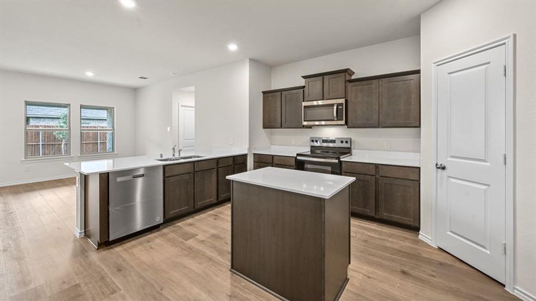 Kitchen with a peninsula, stainless steel appliances, a center island, dark wood finish cabinets, and recessed lighting