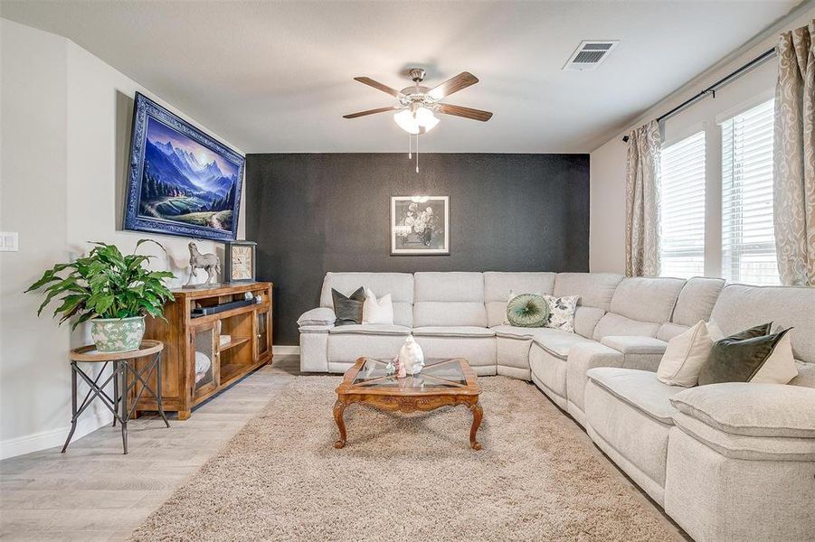 Living area with an accent wall, wood finished floors, a ceiling fan, visible vents, and baseboards