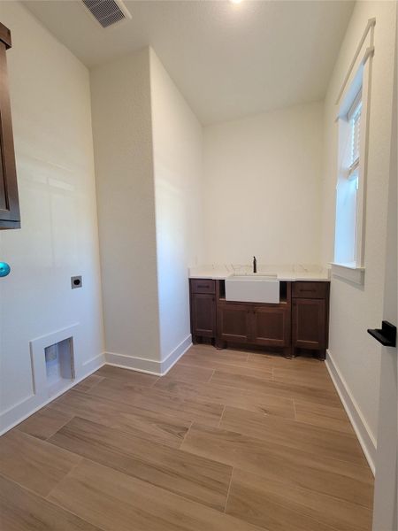 This photo shows a spacious laundry room with light wood-like tile flooring, a farmhouse-style sink with dark cabinetry, and a window for natural light. This photo shows a spacious laundry room with light wood-like tile flooring, a farmhouse-style sink with dark cabinetry, and a window for natural light.