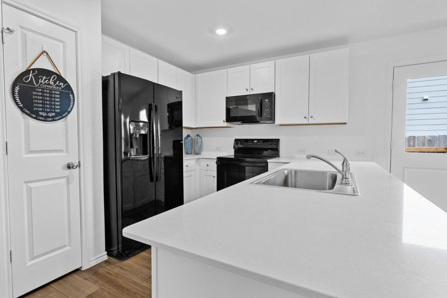 Modern kitchen featuring white cabinetry, black appliances, light wood-finish flooring, recessed lighting, and a stainless steel sink with a gooseneck faucet